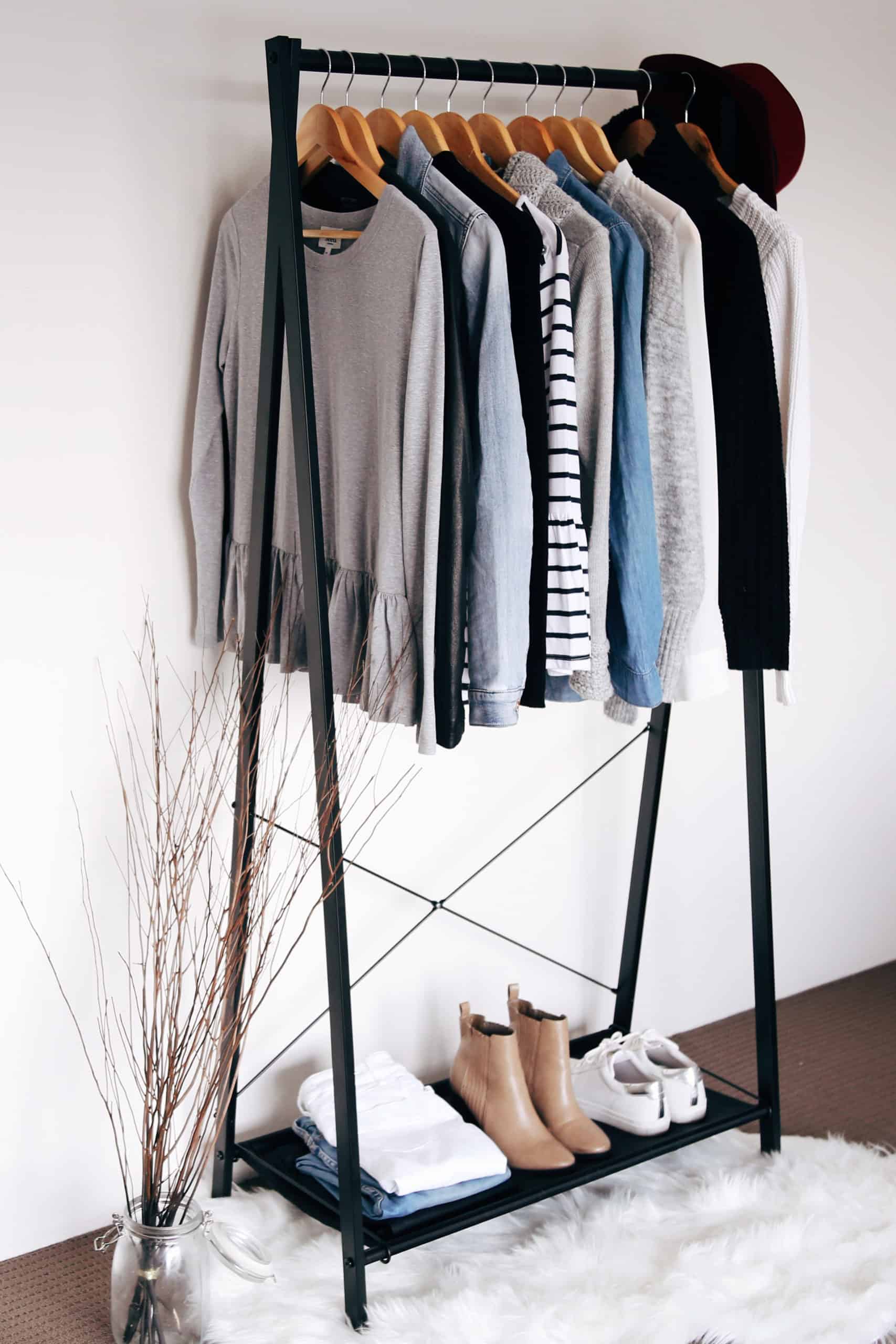 Clothes rack holds multiple sweaters, shoes, jeans and a hat.
