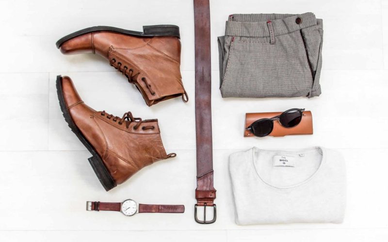 Birdseye view of clothing, boots, a watch, a belt, glasses and a purse.