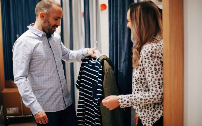 Hayley Cooper inspects clothes in a changing room with a male client.